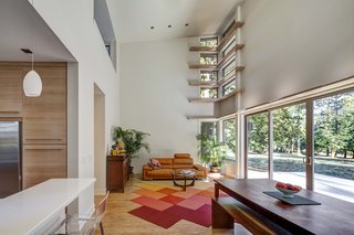 Four rows of narrow "light shelves," a stylistic signature of Stillwater Dwellings, wrap around a corner wall in the double-height living room. A modular carpet by FLOR covers eucalyptus planks from Cali Bamboo. The leather Violino sofa was purchased at an overstock warehouse.