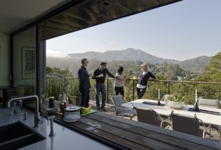 After deeming the original structure unfit for renovation, Chris worked with the couple to raze it and rebuild. With the addition of a lower level, the top floor now sits higher, with clarified sight lines. In the kitchen, a pass-through window connects to the deck, where the couple often entertain; Chris, Jack, Ellen, and Lara Deam enjoy the view. 