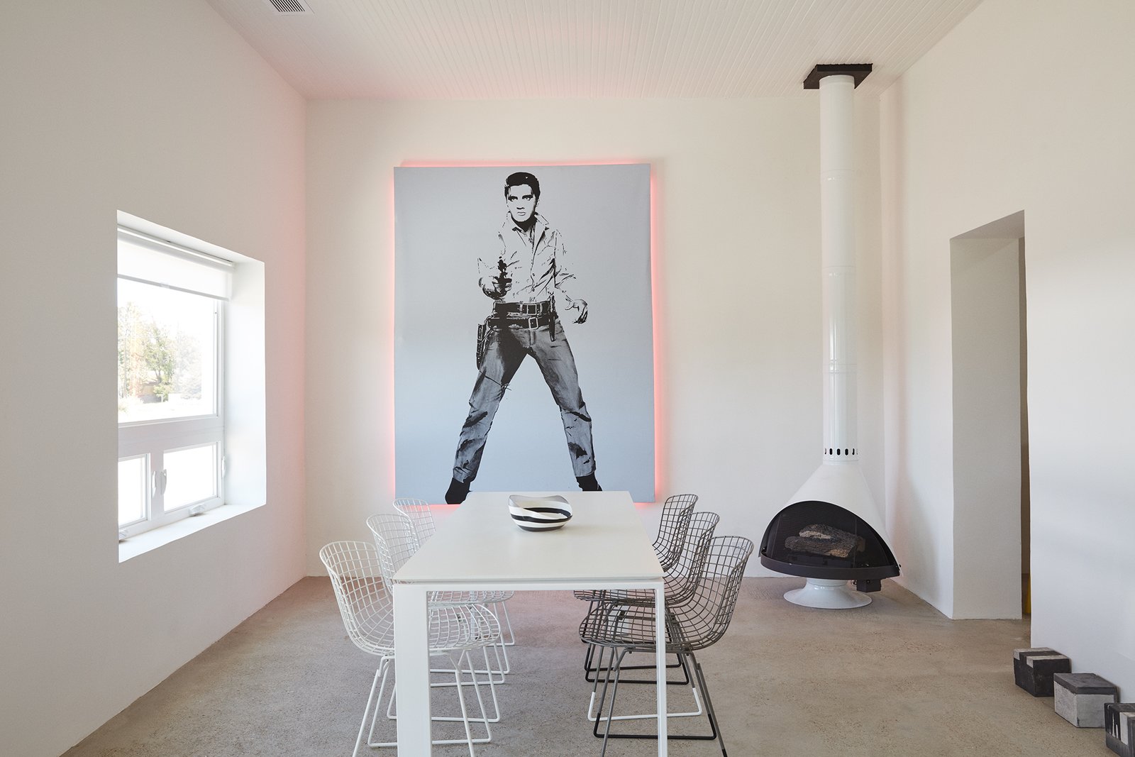 "Everything out here has been something else," designer Barbara Hill says of Marfa, Texas. It’s certainly true of her casita, which was formerly a grocery store: The 1,200-square-foot home is filled with reworked pieces, including <br>the Elvis artwork she embellished with pink lights fabricated by the Neon Gallery in Houston and the <br>refurbished Bertoia chairs from <br>Cast + Crew. The minimal color <br>palette is echoed in the freestanding <br>Malm fireplace and the concrete floor sculptures by William Vizcarra from Wrong Marfa. &nbsp;