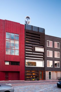 A Passive House in the Netherlands Embodies 5 Tips to Consider When Planning Your Own - Photo 5 of 5 - A technique was used for the wood front of the house called shou-sugi-ban, a traditional Japanese technique that burns cypress wood in order to make it more sustainable. The wood is layered with bright orange planks. Solar collectors, which consist of double-glass tubes that minimize heat loss, form a cornice on the front facade of the house. A wind turbine is on the roof. 