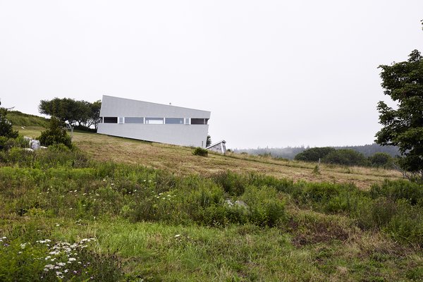 Imagined as a jewel box on a hill, Sliding House takes the place of a barn that once stood on this Nova Scotia site. Its form follows the slope of the land, while the windows are parallel with the horizon, setting up a tension between a plumb interior and a slanted exterior. The tilt of the structure isn’t just a visual trick—it also helps the roof to drain. When the distinctive windows are lit from within, the house serves as a beacon for local sailors. Photo of Sliding House modern home