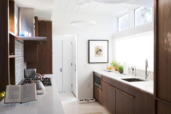 Modern home with kitchen and wood cabinet. Sliders: At the back of the house, floor-to-ceiling LaCantina sliding doors replaced glass panes with a transom and clerestory above, enhancing the link between indoors and out. The residents wanted to stay true to the spirit of the midcentury house and felt that the architects Curtis and Davis would have embraced the technology if it had existed when the house was built in 1953. Photo 11 of Emerald Street Residence