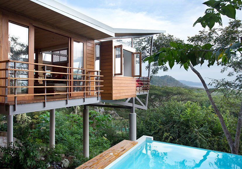 The Floating House stands above the jungle canopy of Costa Rica and was designed by architect Benjamin Garcia Saxe. It's a short walk to the beach and offers elegance that's rooted in nature and simplicity. The structure is made up of three pods that are connected by elevated, outdoor bridges and walkways. Teak flooring and furniture add natural warmth to the main living areas, which are connected to two upstairs bedrooms and an open-air spa bathroom via a 78-foot walkway. The home also features a lounge framed by Concertina floor-to-ceiling glass doors with expansive views of the ocean and jungle.