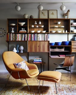 How to Update a Midcentury Modern Gem - Photo 7 of 12 - Illuminated by track lighting, a teak wall unit by Poul Cadovius showcases pottery by Eva Zeisel and Paul McCobb, among others. The desk seat is a T chair by William Katavolos, Ross Littell, and Douglas Kelley; the Womb chair is by Eero Saarinen for Knoll. 