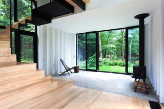 The addition rises above the original shack's 400-square-foot concrete foundation, which is partially visible in the living room. A Cricket patio chair by Hershy Way is used for indoor seating opposite a Morsø wood-burning stove. 