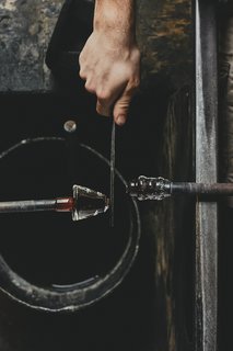 Master Glassmaker Simon Pearce's Sustainable Factory in Vermont - Photo 11 of 16 - Applying The Pontil Next the pontil is affixed to the base, using a tweezer-like tool called the "jacks" to separate it from the pipe.