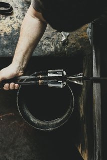 Master Glassmaker Simon Pearce's Sustainable Factory in Vermont - Photo 15 of 16 - Finishing The rim is then finished using a pair of jacks wrapped in wet newspaper, which enables the blower to feel the molten glass while shaping it. 