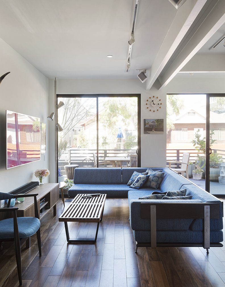 In the living room, a vintage Danish chair faces a sectional upholstered  in Knoll fabric. The Nelson Ball clock is from Vitra and the throw pillows include a Jonathan Adler Seahorse design. Acacia flooring from Reward Hardwood Flooring was used throughout.