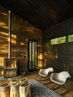 A Rustic-Modern Cabin Inspired by Japanese Bungalows and Shou Sugi Ban - Photo 1 of 12 - A little cottage in North Carolina is furnished with a cluster of wood-stump end tables by Urbia, two Eames rockers, and a 16-H wood-burning stove by Stûv.