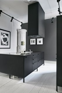 A Careful Renovation of a 19th-Century Flat in Gothenburg Brings it Back to Life - Photo 7 of 11 - The kitchen’s matte-black Vipp system is paired with an antique white ceramic tile stove that was typical in the late 19th century. Although it’s not operable, the stove is used by the couple as a staging ground for illuminated candles and a storage space for an iPad that controls the home’s sound system. 