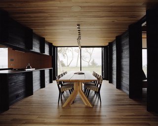 Plagued Ash Trees Were Repurposed to Create This Charred-Cedar Clad Home on Lake Michigan - Photo 8 of 9 - The dining area features an ash table designed by Desai Chia and created by Gary Cheadle. The chairs are by Jens Risom. 
