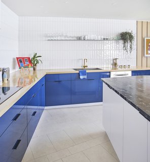An Interior Designer Helps His Mother Turn Her 1960s Chicago Apartment Into a Colorful Haven - Photo 3 of 8 - A wood countertop with blue laminate cabinets underneath contrasts with a white island topped with travertine. The wall tile is Origin Birch White by AKDO, and the brass faucet is by California Faucets. As in the rest of the apartment, the flooring is colored cork from Globus Cork. 