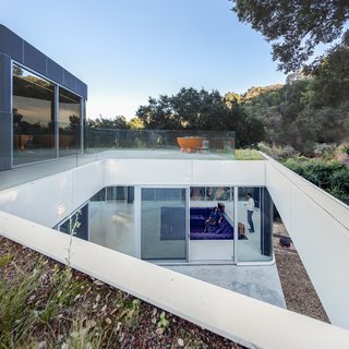 The Conversation Pit Makes a Much-Appreciated Comeback at an Ultramodern Home in Cupertino - Photo 6 of 9 - A bridge of steel grating leads to the garage and the entrance, both on the upper level. Sunlight funnels through an opening in the rooftop down to the living area. The orange hot tub is by ALFI. 