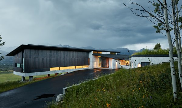 The driveway entrance introduces the stately side of the home, displaying clean lines made of concrete and Cor-Ten steel. Almost every material implemented in this home was done so to create a maintenance-free space that withstands the weather and betters with age. The design required minimal alteration of the site, a notable accomplishment in land preservation. To maintain the natural grade, the structure is elevated and cantilevered at the slope, held up by columns which needed only a small amount of foundation work. The only major land disturbance occurs in the recessed garage, which has been supplemented with a green roof on top to preserve the meadow. Photo of Wyoming Residence modern home