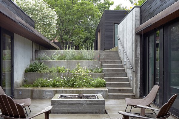 A stepped concrete garden planted with herbs and flowers marks the descent to the house. The courtyard is the focal point of the U-shaped structure; there is clear visibility between the kitchen on one side and the children's bedrooms on the other.