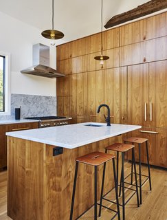 You Won't Lose Your Wi-Fi Connection at This Hamptons Retreat - Photo 4 of 6 - European walnut lines the custom kitchen, which is outfitted with Blum and Hafele hardware, a Solna faucet by Brizo, and pendants by Danish studio Frama. The range is Thermador.