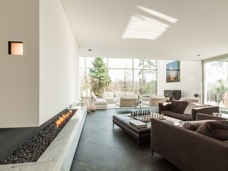 Proof That a Modern Fireplace Can Be the Defining Factor of a Space - Photo 2 of 7 - Built in 2011, this six-bedroom, five-bath villa in Brussels offers an array of spaces complete with high ceilings, expansive terraces, and a meticulously landscaped garden. Running adjacent to a wall of floor-to-ceiling windows is a cut-in stone fireplace that lies beneath a glass-enclosed walkway. 