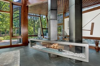 Proof That a Modern Fireplace Can Be the Defining Factor of a Space - Photo 4 of 7 - Designed by architect David Jameson in the heart of Bethesda, Maryland, this sculptural residence is filled with bespoke elements that are made up of wood, metal, stone, and glass. The centralized fireplace divides the open living space into two separate seating areas, without closing them off from one another. 