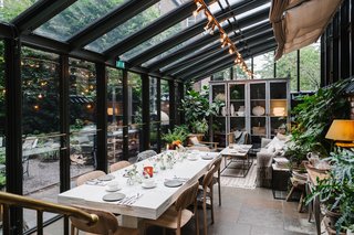 A Visual Journey Through Stockholm's Hotel Ett Hem - Photo 7 of 12 - Crawford created a covered patio addition where guests can relax and enjoy a meal within the garden. The leafy glass house holds modern wood furnishings and cozy textiles.