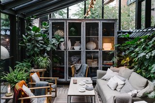 A Visual Journey Through Stockholm's Hotel Ett Hem - Photo 10 of 12 - Shown here is the lounge seating vignette in the covered patio/garden area, which is filled with greenery and furniture that's covered with warm textiles.