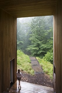 A Cypress-Clad Lake House Posted Up on an Old Logging Road - Photo 4 of 4 - A small courtyard cut out of the center holds a sheltered terrace with an outdoor fireplace. This open area separates the main living spaces from the bedrooms and creates a framed view for the family.<span> <a href="/discover/dwelllpow">#dwelllpow</a></span>