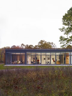 The glass-enclosed side of the house reveals a screened porch on the left, followed by a combined open area that brings together the living space, dining area, and the kitchen. 