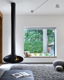 From Front to Back, This Toronto Home Literally Merges Heritage and Modernism - Photo 2 of 3 - The living space that features a freestanding fireplace looks out through a seated window that perfectly frames the yard. 