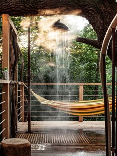 Outside, on the wooden deck, a hammock invites guests to take a break and unwind; an open-air tree shower offers the perfect opportunity to freshen up after exploring the forest, just before enjoying a meal prepared on the barbecue or a pizza baked in the wood fired pizza oven. A spiral staircase leads to the top level where a hot tub and a sauna provide the ultimate relaxation experience among ancient oak trees.
