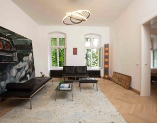 A Hidden Passageway Makes Each Room in This Berlin Flat a Private Destination - Photo 1 of 6 - An antique floor lamp and signage pair with an oversize automotive painting and a rug by Rugstar in the main living space. The daybed and lounge chairs are from Norr11's Man seating collection; the pendant is from Cameron Design House.