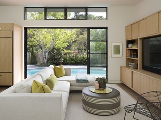 Sliding glass doors connect this renovated home in Marin County to a rear terrace and kidney-shaped pool. The sectional sofa is custom by Mansfield + O’Neil Interior Design. 