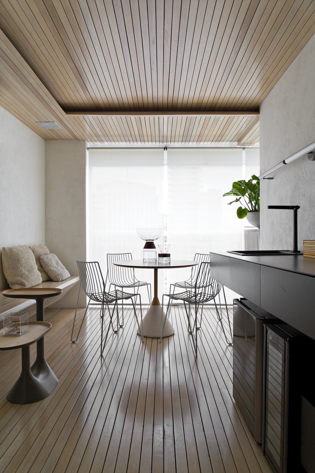 A Brazilian Bachelor Pad Embraces Light and Darkness The dining area between the living room and balcony is the most light-filled space in the common area. The floors, lining, and bench were built using solid wood ripada.