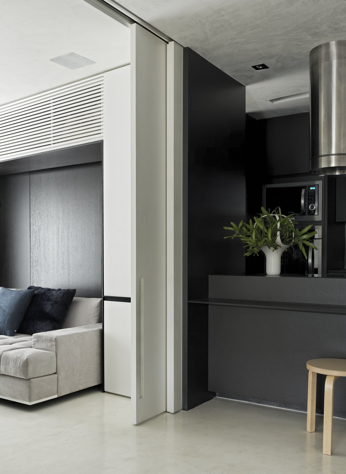 A Brazilian Bachelor Pad Embraces Light and Darkness A sliding door to the guest bedroom makes this flexible area even more accessible. A burnt cement floor connects this room to the kitchen.