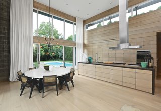 A Sputnik chandelier in aged steel from Restoration Hardware hangs above a custom concrete-topped table. The vintage cane-and-teak dining chairs were designed in 1966 by Pierre Jeanneret. In the kitchen, a brushed stainless-steel range hood by Modern-Aire is matched with faucet hardware from Dornbracht, a Blanco sink, Viking rangetops, and built-in ovens by Wolf. Recessed lighting overhead uses LED bulbs set in Juno housing. 