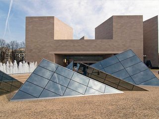The East Wing of the National Gallery of Art sits adjacent to the museum's original neoclassical home, both contrasting and complementing the original gallery. Built to house the National Gallery of Art's modern art collection, the structure is composed of triangular shapes, with corners of the stone-clad main building rising high to produce an abstract turret-like effect. A triangular paneled glass roof covers the central atrium that connects the two buildings. 