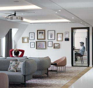 Take a Peek Inside Airbnb's New Loft-Inspired Office Space in Paris - Photo 8 of 13 - Inspired by local landmark Opera Garnier, the custom carpet in the hospitality lounge includes traditional patterns often found within Opera Houses. This traditional design element is juxtaposed with contemporary furniture and a gallery wall of artwork that references Airbnb, travel, and the opera.
