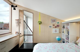 A 1960s Melbourne Warehouse Is Upcycled and Transformed Into an Energy-Efficient Family Home - Photo 6 of 11 - This little bedroom in a plywood pod looks out to the roof-deck and features angled ceilings and strategic lighting that's hidden above a shelving unit.