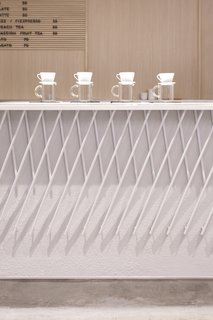 A Sleek Coffee Shop in Hong Kong With Beautiful, Minimalist Interiors - Photo 3 of 9 - The front of the coffee bar features a decorative armor made out of angled pieces of white-painted metal that form a criss-cross pattern.