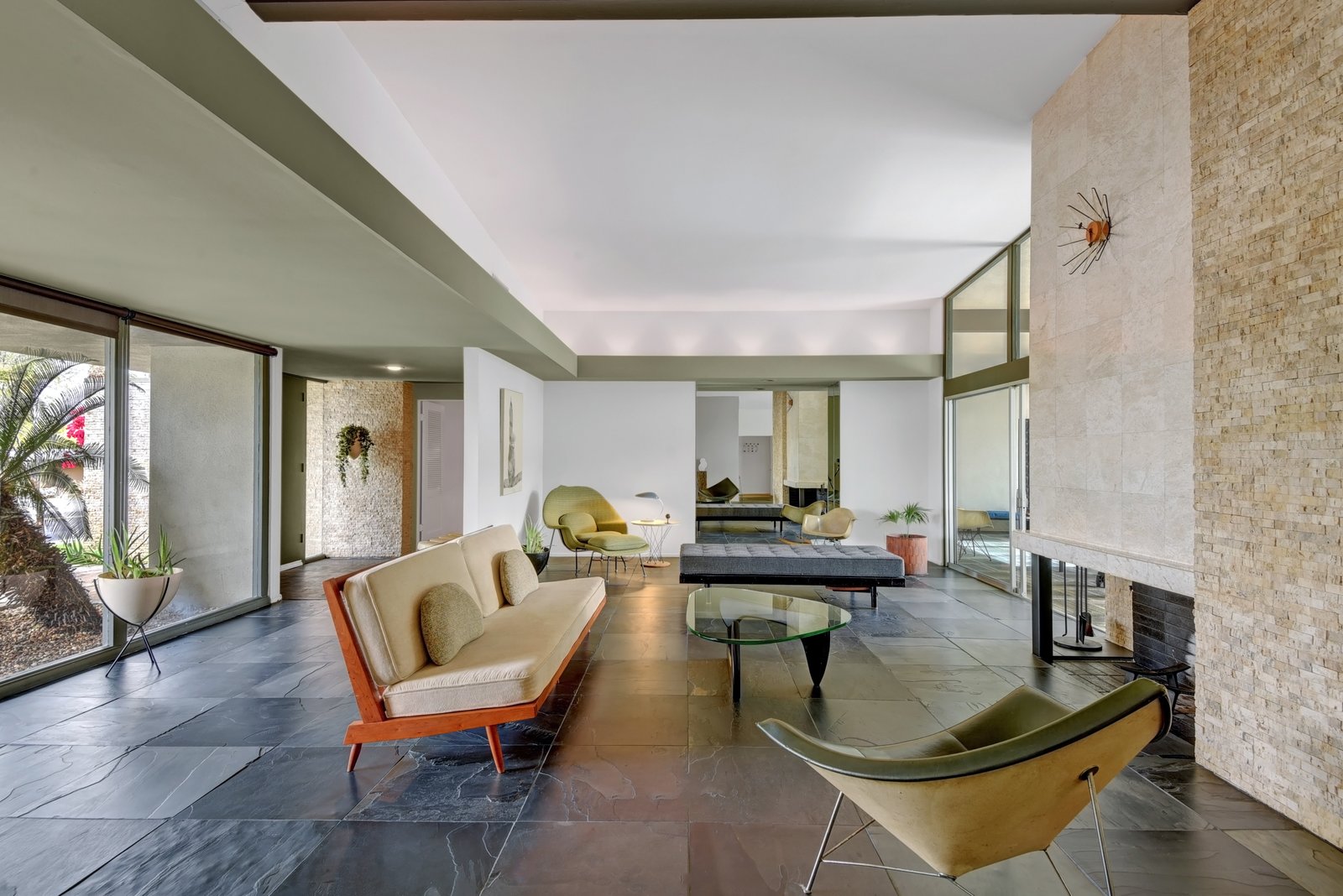 The interiors fully embrace the midcentury aesthetic, with high-beamed ceilings, slate floors, custom wood flooring, and a split rock fireplace.
