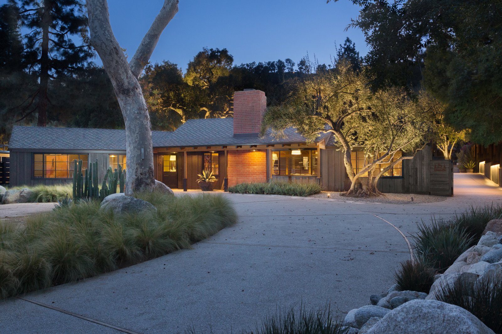 The outdoors is easily accessed from every room, showcasing a mix of large specimen trees, drought tolerant plants, and decomposed granite and river rock.