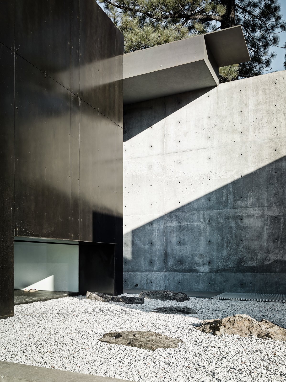 A layering of spaces - a concrete wall that leads to a rock garden that leads to a window.
