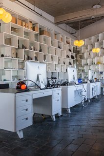 Inside the Head Office of Bocci - Photo 4 of 7 - White metal desks are lit by a desk lamp variation from Bocci's 28-series. Behind them, open bookshelves act as room dividers.