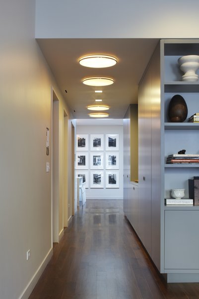 The front hallway links the living room to the kitchen and dining area. The existing apartment was originally a manufacturing loft space. NYC lofts being long and narrow with windows typically only at the front and rear façades can be somewhat dark. With this in mind we designed the apartment to have light filled spaces via rooftop skylights. Here a photo series by Bernd and Hilla Becher are washed with natural light from a large drum skylight not yet visible from this perspective. The hallway ceiling echoes the drum skylight with Munkegaard fixtures, one of our favorites from Louis Poulsen. Photo 13 of White Street Residence modern home