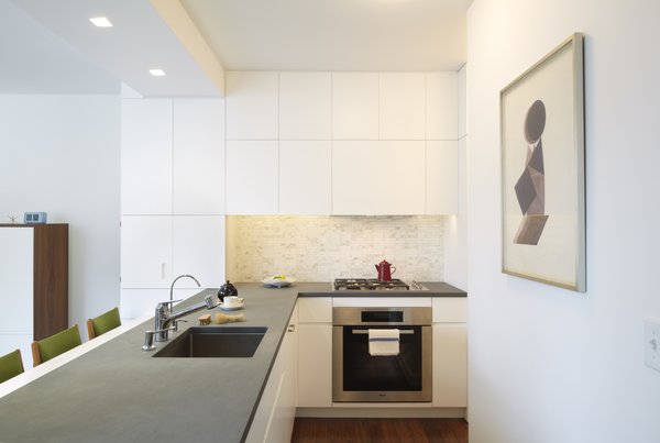 One of the details you can see throughout all of our projects is the concealment of the electrical outlets for the countertop appliances. This is accomplished by routing a GFCI outlet strip into the underside of the upper cabinetry. The detail keeps the tile free of duplex receptacles allowing the beauty of the backsplash to read uninterrupted. The kitchen backsplash is Calacatta mosaic tile - a splurge in an otherwise tight construction budget. Photo 14 of Riverside Residence modern home