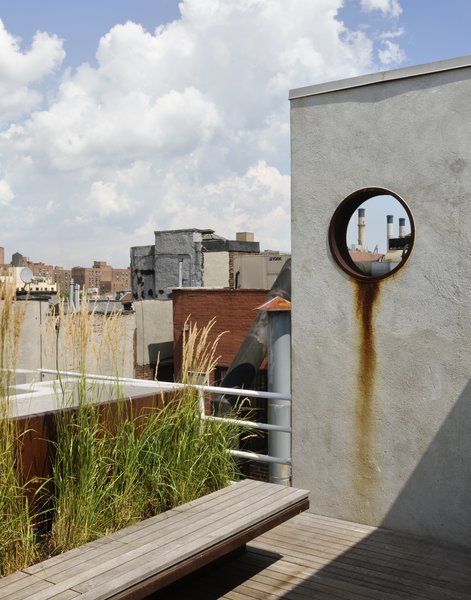 The garden is accessed from a rooftop penthouse designed by pulltab and built two years earlier. A large diameter steel pipe was cut and placed into a new stucco wall. This aperture frames a view to a power plant located on the Lower East Side. The steel ring was left unpainted so it can rust and bleed down the wall. The floating bench is made from Cor-Ten steel and teak which is left to weather a beautiful grey. Photo of East Village Roof Garden modern home