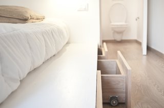The subdivided apartment initially lacked storage capacity. Slide-out drawers under the bed, as well as placing the television in what was formerly the fireplace, helped stretch the space to make the apartment more livable. 