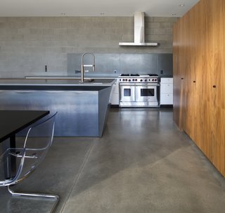 This Sleek Desert Home Seems to Melt Into the Sky - Photo 5 of 12 - The downstairs communal living spaces flow freely between kitchen, dining room, and living room. Concrete block walls and polished concrete floors emphasize the heavy materiality that supports the visual lightness of the upper story.