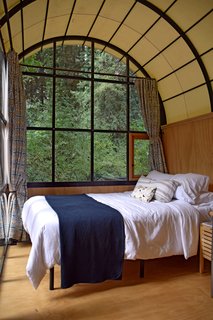 The curved ceiling of the accessible suite amplifies the spacious feel imparted by the glass facade. Custom curtains, blown glass fixtures, Douglas fir cabinetry with custom steel handles, and a marble-tiled bathroom are just some of the components in this elegant hut. 