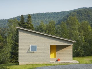 A Mini-Home With Mega-Views - Photo 1 of 4 - A cutaway in the structure's cubic shape forms a front porch, where a graphic yellow door welcomes visitors. The roof slopes downwards, holding more intimate spaces at its lower end. 