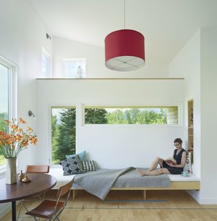 A Mini-Home With Mega-Views - Photo 3 of 4 - A pine interior subtly frames each window opening to accentuate views without obstructing them. The light material palette in the home contributes to a sense of airiness. Local maple planks on the floor have been cut to shorter lengths and laid perpendicular to the view, giving it a fluid effect. A camouflaged hatch door leads to the basement level, which acts as a storage and laundry area. 