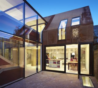 Weathered Steel Clads a $4.7M Home Near London’s Kew Gardens - Photo 4 of 10 - A flight above the living room, a kitchen and dining area opens onto a walled rear courtyard. The wing also includes a pantry, a walk-in closet, laundry room, and bathroom.